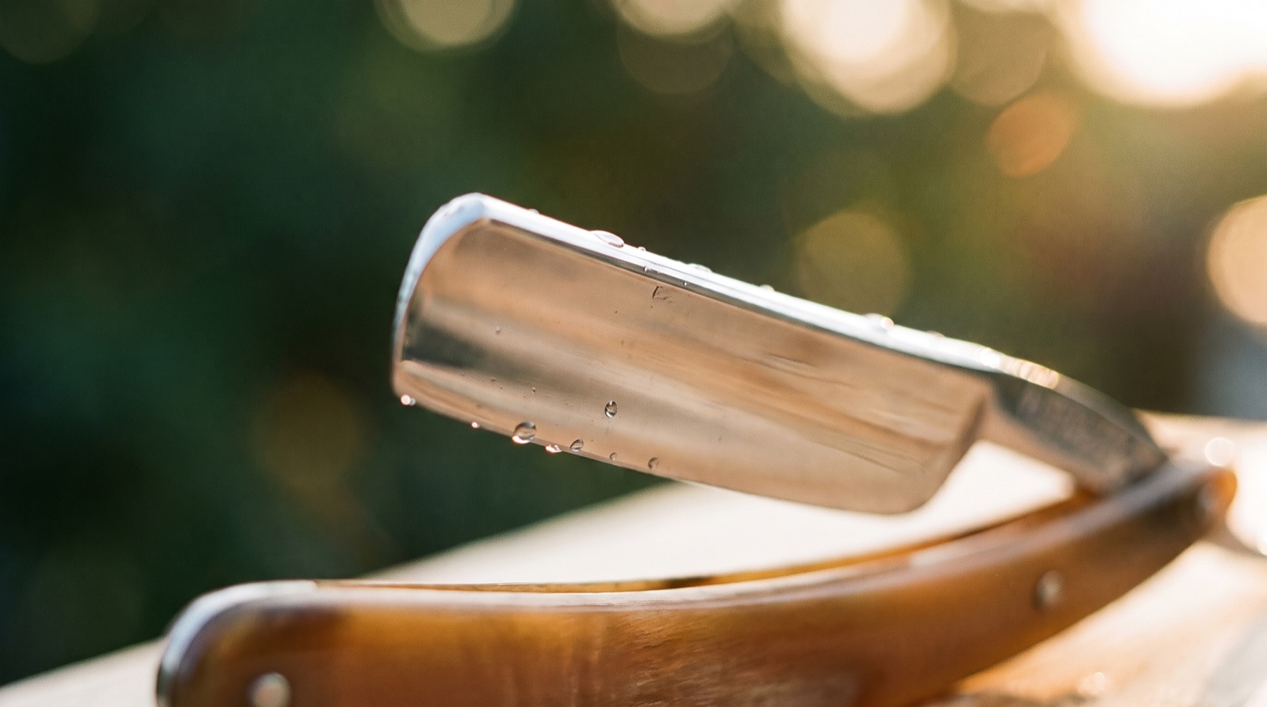 A classic straight razor catching warm light, the tools of a proper barbershop